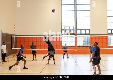 Joueur de volley-ball masculin asiatique sautant près du volley-ball à pointes de filet dans la salle de gym sous les fenêtres Banque D'Images