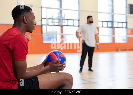 Divers coéquipiers masculins se reposant sur un banc de terrain tenant un filet d'observation de volley-ball rouge bleu Banque D'Images