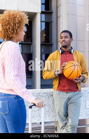 Divers amis appuyés contre la rampe de pierre à plaza tenant basket-ball, valise, espace de copie Banque D'Images