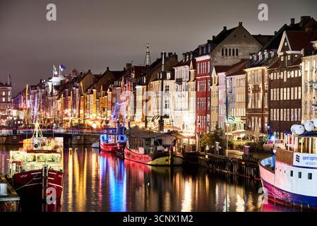 Nyhavn la nuit : des reflets vibrants scintillent sur le canal, avec des bâtiments historiques colorés et des bateaux éclairés bordant le front de mer. Copenhague, Danemark Banque D'Images