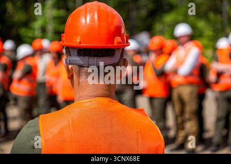 Constructeurs dans des gilets réfléchissants, casques durs debout ensemble sur le chantier de construction. Groupe de constructeurs en casques de sécurité et gilets réfléchissants. Banque D'Images