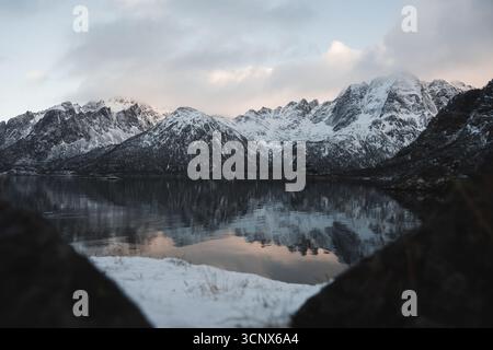 Scène hivernale sereine dans les îles Lofoten, en Norvège, avec de majestueuses montagnes enneigées et leurs reflets dans des eaux calmes, créant un calme Banque D'Images