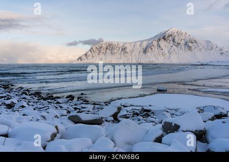 La côte enneigée et les montagnes majestueuses rencontrent la mer sereine dans cette scène hivernale des îles Lofoten, en Norvège. La beauté tranquille évoque un Banque D'Images