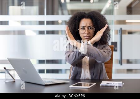 Portrait d'une femme d'affaires afro-américaine assise à un bureau dans le bureau et montrant un geste d'arrêt à bras croisés à la caméra. Banque D'Images