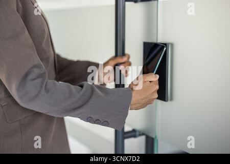 Photo en gros plan d'une partie du corps, mains d'une jeune femme afro-américaine entrant dans le bureau, ouvrant la porte automatique avec une clé électronique à travers le téléphone. Banque D'Images