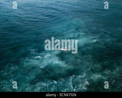 Vue aérienne d'un surfeur solitaire au milieu des vagues turquoise mousseuses, une figure solitaire contre la vaste étendue de l'océan Indien, Welligama, Sri Lanka. Banque D'Images