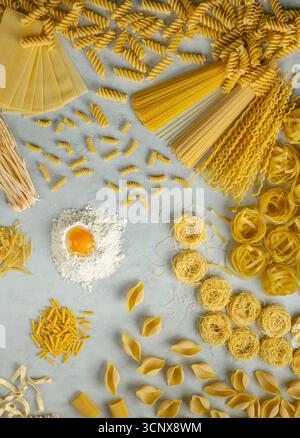 Différents types de pâtes disposées en cercle avec de la farine et du jaune d'œuf au centre, créant une vue aérienne des ingrédients de la cuisine italienne Banque D'Images
