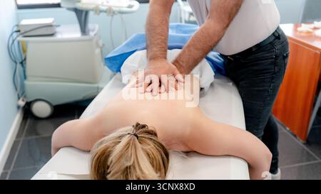 Le physiothérapeute masculin recadré méconnaissable effectue un massage thérapeutique du dos sur une patiente féminine anonyme dans un cadre clinique, soulignant Banque D'Images