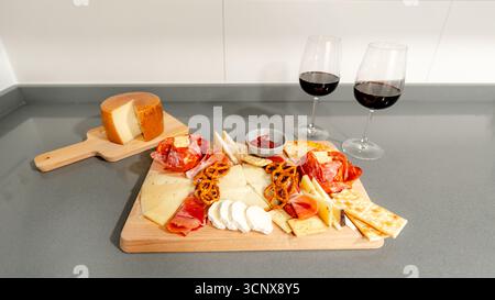Le tableau de charcuterie élégant affiche un assortiment de fromages, viandes, craquelins et bretzels, accompagnés de deux verres de vin rouge, créant une configuration parfaite f Banque D'Images