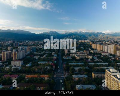 Vue aérienne des routes droites de la ville mènent l'œil aux montagnes enneigées au loin, un mélange de vie urbaine et de beauté naturelle, Almaty, région d'Almaty, Kazakhstan. Banque D'Images