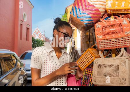 Une femme d'affaires noire explore le marché de rue animé de Cartagena de Indias, en Colombie. Elle admire les sacs tissés faits à la main, reflétant la culture et l'artisan Banque D'Images