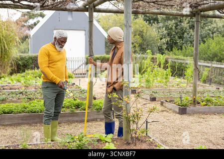 Divers amis masculins travaillant des lits surélevés avec une pelle à manche jaune dans le potager communautaire Banque D'Images