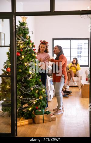Famille diversifiée plaçant des ornements rouges et dorés sur l'arbre de noël dans le salon, espace de copie Banque D'Images