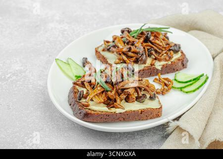 Sandwichs ouverts sains à base de plantes avec champignons Shimeji sautés. Repas végétalien riche en protéines est servi sur une assiette blanche, fond de pierre clair, à proximité Banque D'Images