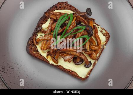 Sandwichs ouverts sains à base de plantes avec champignons Shimeji sautés. Le repas végétalien riche en protéines est servi sur une assiette blanche, fond de pierre chaud Banque D'Images