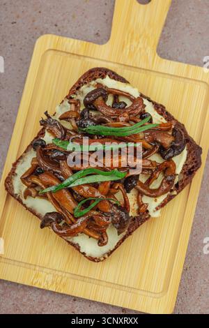 Sandwichs ouverts sains à base de plantes avec champignons Shimeji sautés. Le repas végétalien riche en protéines est servi sur une assiette blanche, fond de pierre chaud Banque D'Images