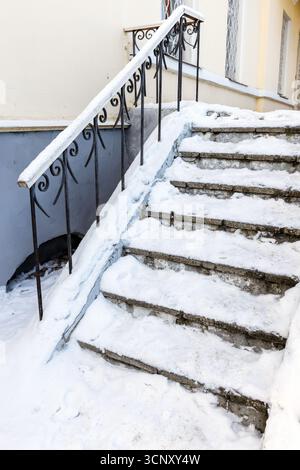 L'escalier en béton recouvert de glace est recouvert de neige fraîche, flanqué d'une balustrade décorative en fer forgé Banque D'Images
