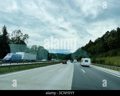 Munich, Allemagne - 24 septembre 2022 : scène routière allemande animée avec des camions et une caravane le long d'une route bordée d'arbres sous un ciel nuageux. Banque D'Images