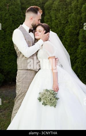 Un couple de jeunes mariés partage un moment intime. Le marié embrasse doucement le front de sa mariée, montrant leur amour et leur bonheur le jour de leur mariage. T Banque D'Images