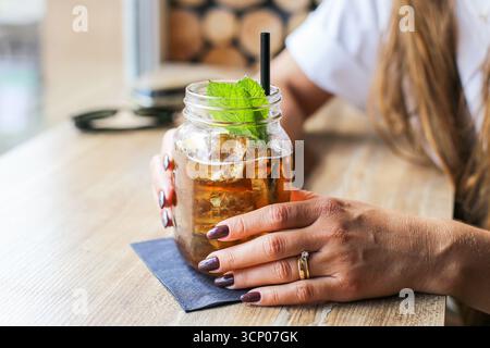 Boisson fraîche rafraîchissante dans un pot mason avec des feuilles de menthe et des glaçons. Femme tenant du verre. Gros plan sur les boissons estivales. Mode de vie sain et détente. Banque D'Images