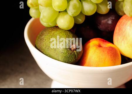 Fruits frais mélangés dans un bol. Avocat avec raisins et pêche. Pomme avec prune et agrumes. Récolte saisonnière naturelle du verger. Banque D'Images
