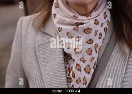 Manteau élégant beige avec écharpe à imprimé léopard et détails minimalistes. Vue rapprochée d'un manteau beige chic complété par une écharpe à imprimé léopard tendance Banque D'Images