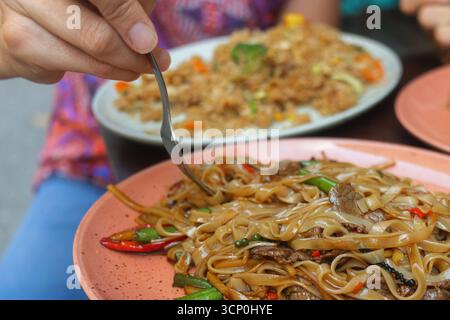Le soir, les convives savoureux dégustent des plats de riz savoureux et frits dans un stand de cuisine de rue thaïlandais animé. Banque D'Images