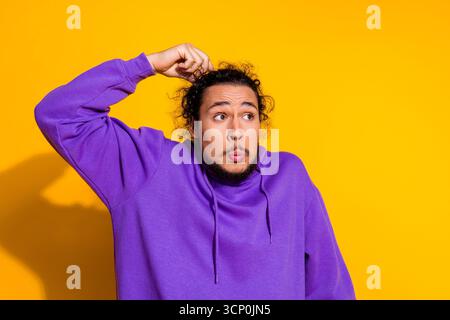 Jeune homme dans un sweat à capuche violet sur fond jaune exprimant un geste représentant la curiosité et l'amusement Banque D'Images