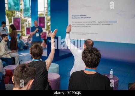 Le public lève la main pendant la session de conférence avec l'orateur sur la scène bleue et le grand écran Banque D'Images