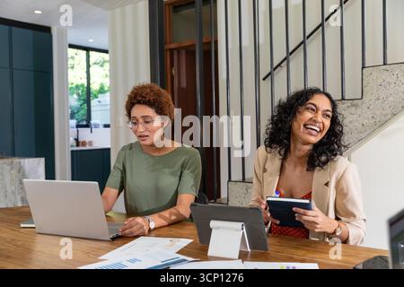 Diverses collègues féminines tapant sur un ordinateur portable, tenant une tablette à la table de bureau à domicile avec des graphiques Banque D'Images