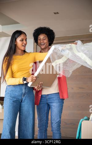 Couple diversifié déballage de l'image encadrée dans le salon à la maison avec du papier à bulles, des boîtes mobiles Banque D'Images