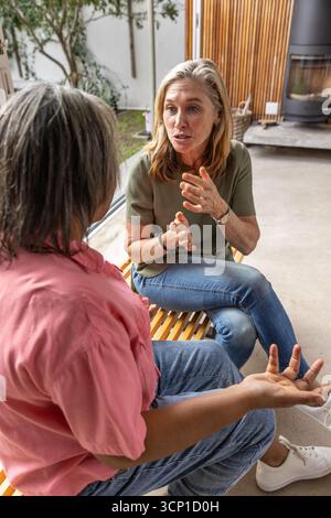 Deux amies parlant animées sur un banc en bois dans le salon avec poêle à bois Banque D'Images