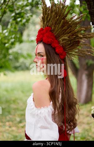 Jeune femme en costume folklorique ukrainien traditionnel avec de longs cheveux, portant une coiffe faite à la main faite d'oreilles de blé et de fleurs rouges Banque D'Images