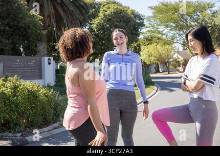 Amies féminines diverses riant bavardant et se réchauffant dans la rue portant des baskets et une montre de fitness Banque D'Images