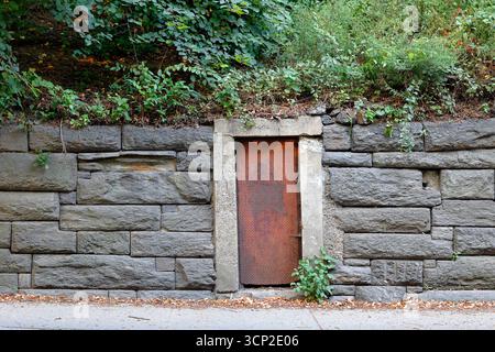 Une porte en tôle d'acier rustique abandonnée dans un mur de pierre de granit le long de la transversale de la 86e rue dans Central Park de Manhattan, New York City. Banque D'Images