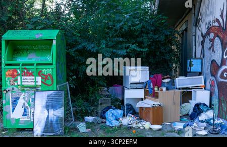 Les ordures ménagères et les déchets encombrants empilés à côté de la poubelle des dons à Berlin, symbolisant la négligence et la dégradation urbaine dans l'espace public. Banque D'Images