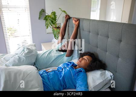 Couple diversifié couché dans la chambre sur le lit avec tête de lit touffetée, étirement, repos Banque D'Images