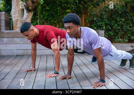Divers amis masculins tenant des positions de planche sur le pont en bois dans le patio arrière avec smartwatches Banque D'Images