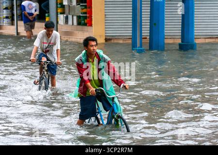 Des hommes philippins locaux faisant du vélo dans une rue inondée après de fortes pluies à Manille, Philippines Banque D'Images