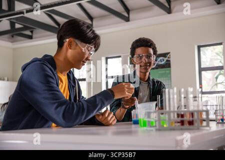 Divers étudiants adolescents mélangeant des liquides et réglant des béchers sur une paillasse de laboratoire avec portoir à tubes Banque D'Images