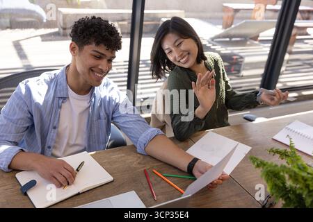 Divers collègues examinant la carte imprimée au bureau à table avec ordinateur portable, cahiers et fougère en pot Banque D'Images