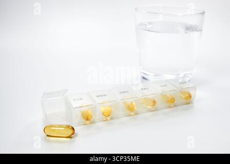 Un organisateur hebdomadaire de pilules montrant un dosage quotidien de suppléments de gélules jaunes comme l'huile de poisson ou la vitamine E. Un concept pour la gestion de la santé, routine quotidienne Banque D'Images