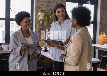 Diverses collègues féminines collaborant au bureau avec un mur de briques à l'aide de tablettes et de stylets Banque D'Images