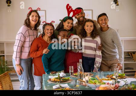 Famille élargie diversifiée célébrant repas dans la salle à manger à la table à manger avec des bougies, bandeaux Banque D'Images