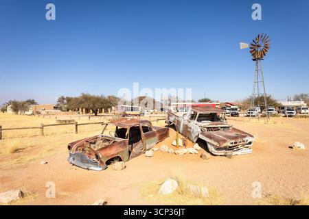 Cimetière de voitures de Solitaire en Namibie - 27 août, 2025 : présente des voitures anciennes rouillées près de petits bâtiments du désert, contre des dunes et des montagnes, cap Banque D'Images