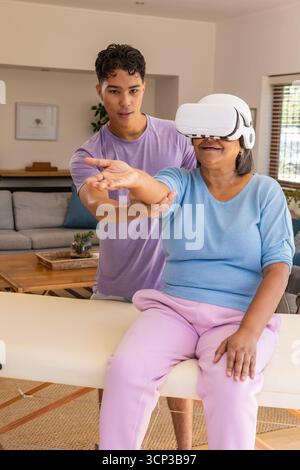 Femme senior atteignant, bras de guidage de soignant masculin sur la table de thérapie à la maison avec casque VR Banque D'Images