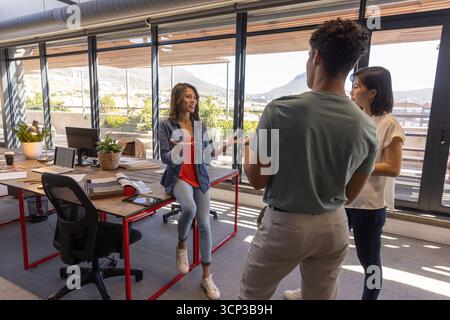 Divers collègues discutant du projet autour du bureau avec ordinateur portable, documents, tasse à café dans le bureau Banque D'Images