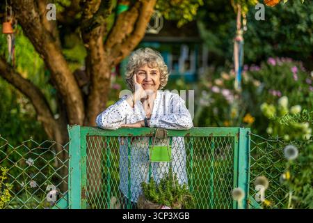 Femme âgée souriante dans son jardin par une journée ensoleillée Banque D'Images