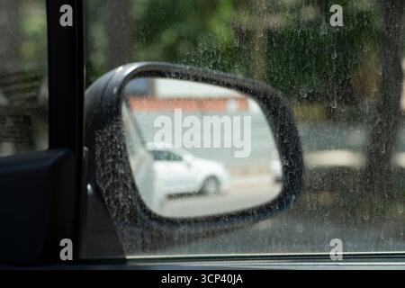 Une fenêtre de voiture poussiéreuse et un rétroviseur latéral reflétant un véhicule blanc par une chaude journée d'été. Symbole de pollution, de temps sec et de chaleur urbaine. Le flou et d Banque D'Images