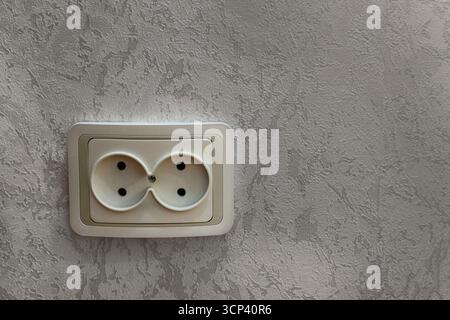 Gros plan d'une prise murale électrique double blanche montée sur un mur en plâtre texturé. La photo illustre l'infrastructure électrique domestique et int Banque D'Images